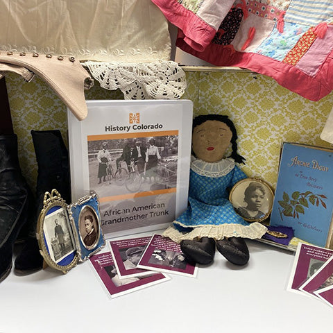 African American Grandmothers educational trunk including black button shoes, binder with teaching materials, a stuffed doll and a book.