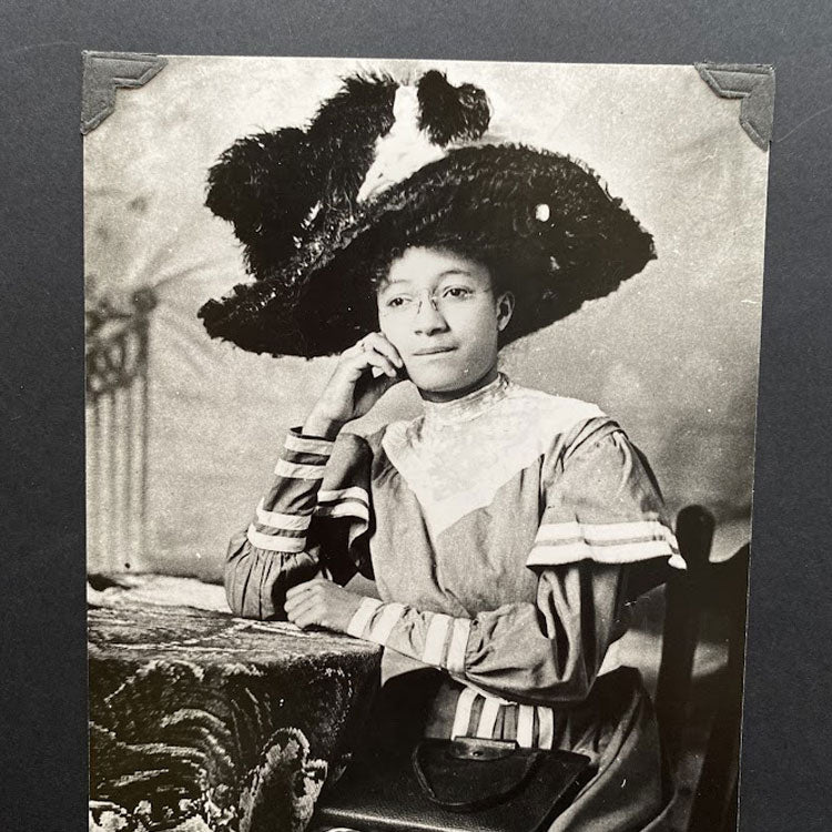 Old photo of a woman in a Victorian style dress and large hat with feathers