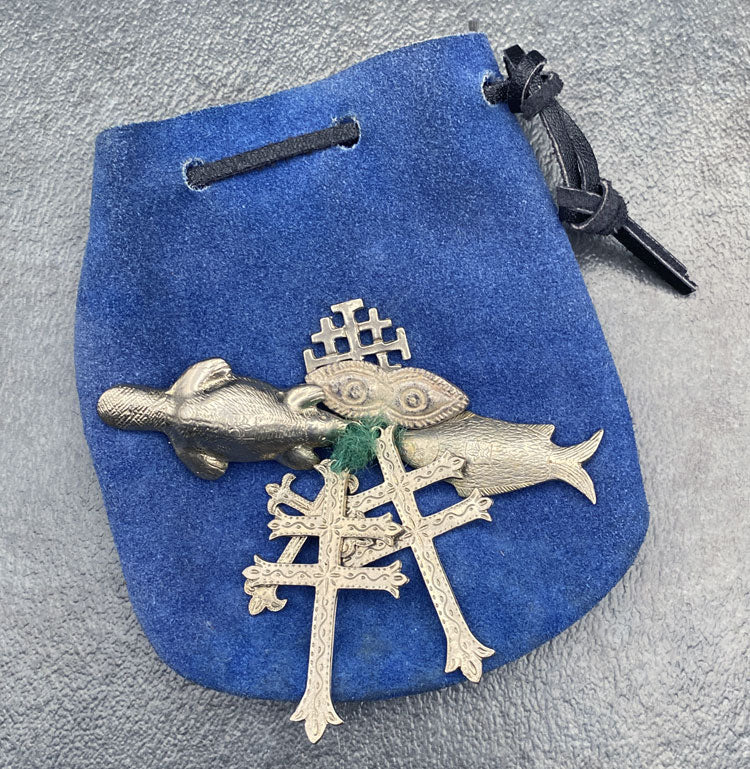 Leather pouch with sliver charms, beaver, fish, and crosses tied together with yarn.
