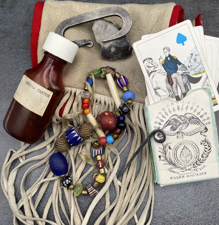 Fringed buckskin mountain man bag with bottle of beaver castor, trading beads, flint and steal, metal pick and deck of playing cards.