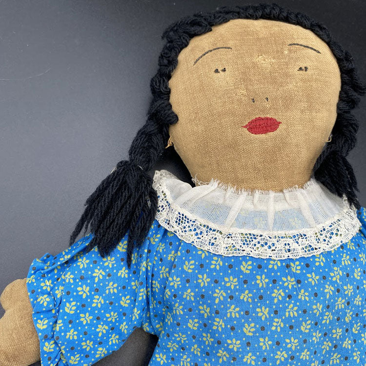 Stuffed doll with burlap fac, blue dress and black yarn hair.