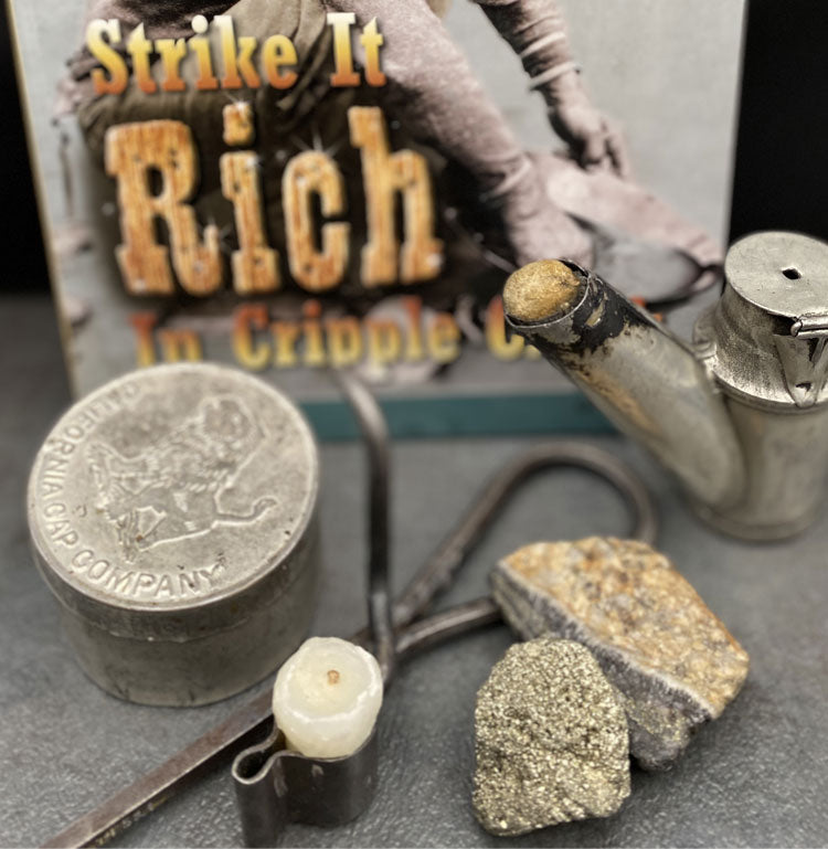Mining tools including candle, lamp, fool’s gold and small tin box and book titled Strike it Rich in Cripple Creek.